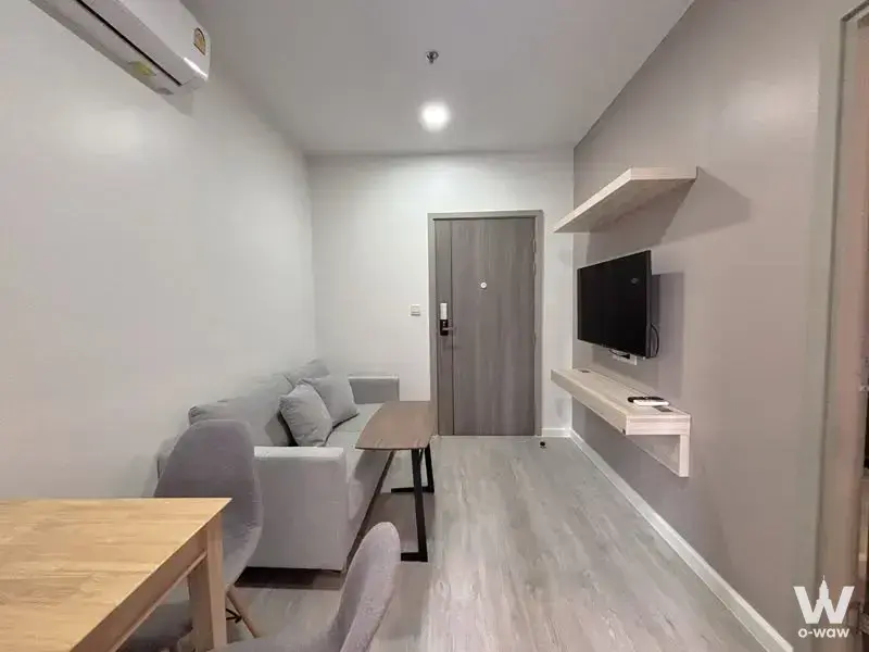 Living area with grey sofa, coffee table, and wall-mounted TV in M Ladprao 1-bed condo