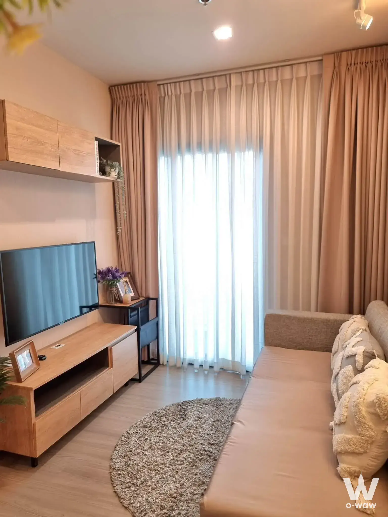 Living room in THE BASE Phetchaburi-Thonglor with beige sofa, TV console, and floor-to-ceiling windows
