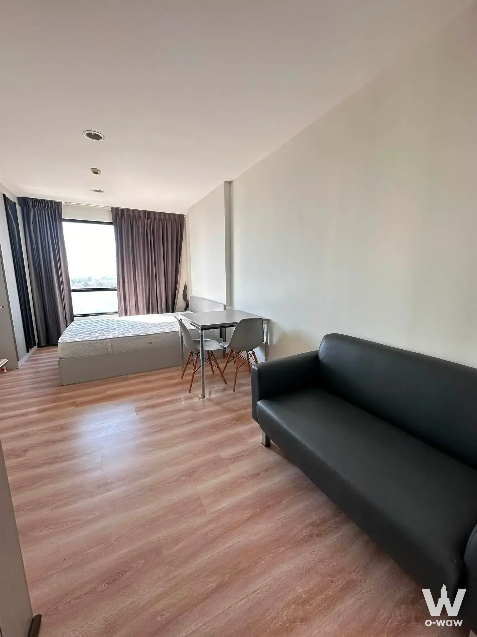 Premio Fresco 1-bed studio with light wood floors, black sofa, and tree-view window
