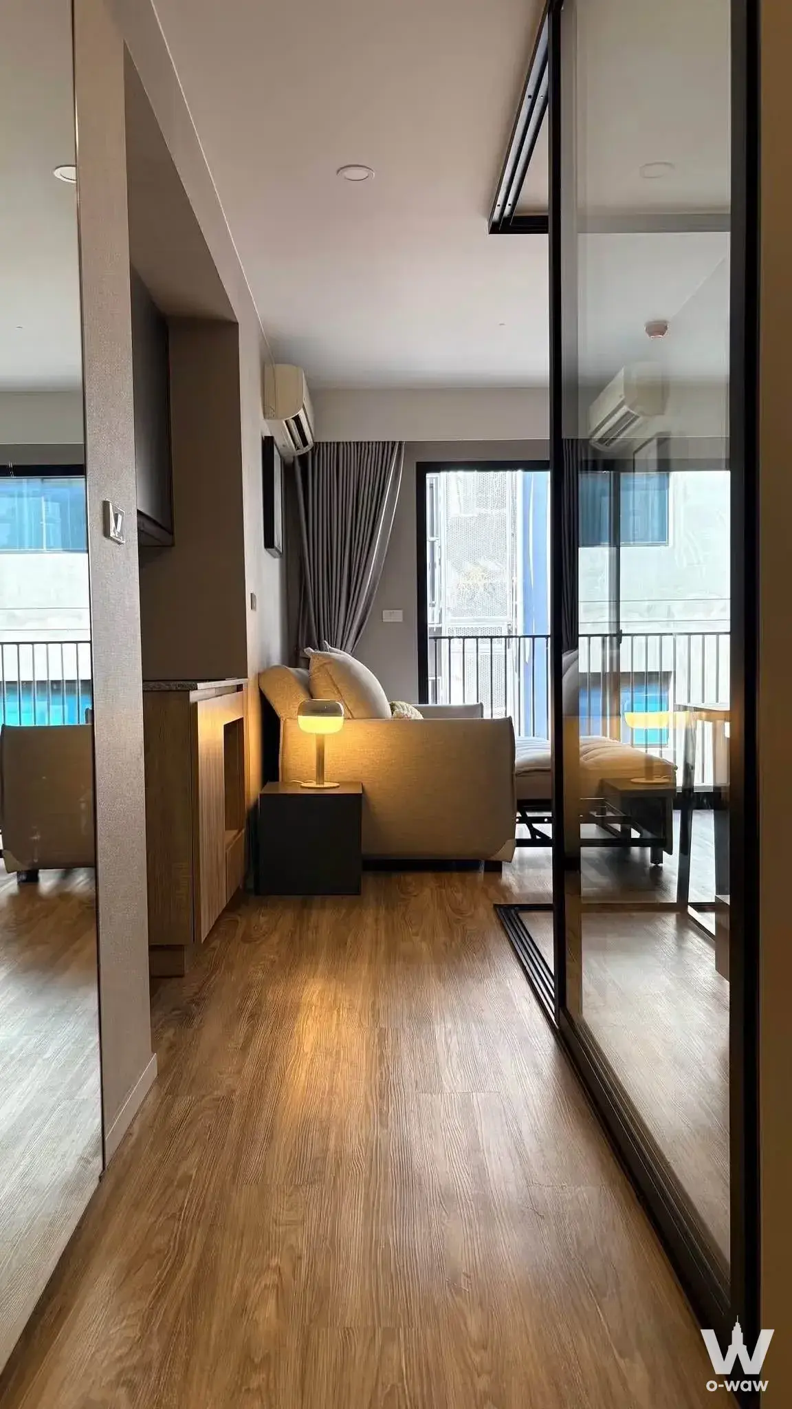 Compact living area in 1-bed Sathon condo with mirrored wall, beige sofa, and balcony