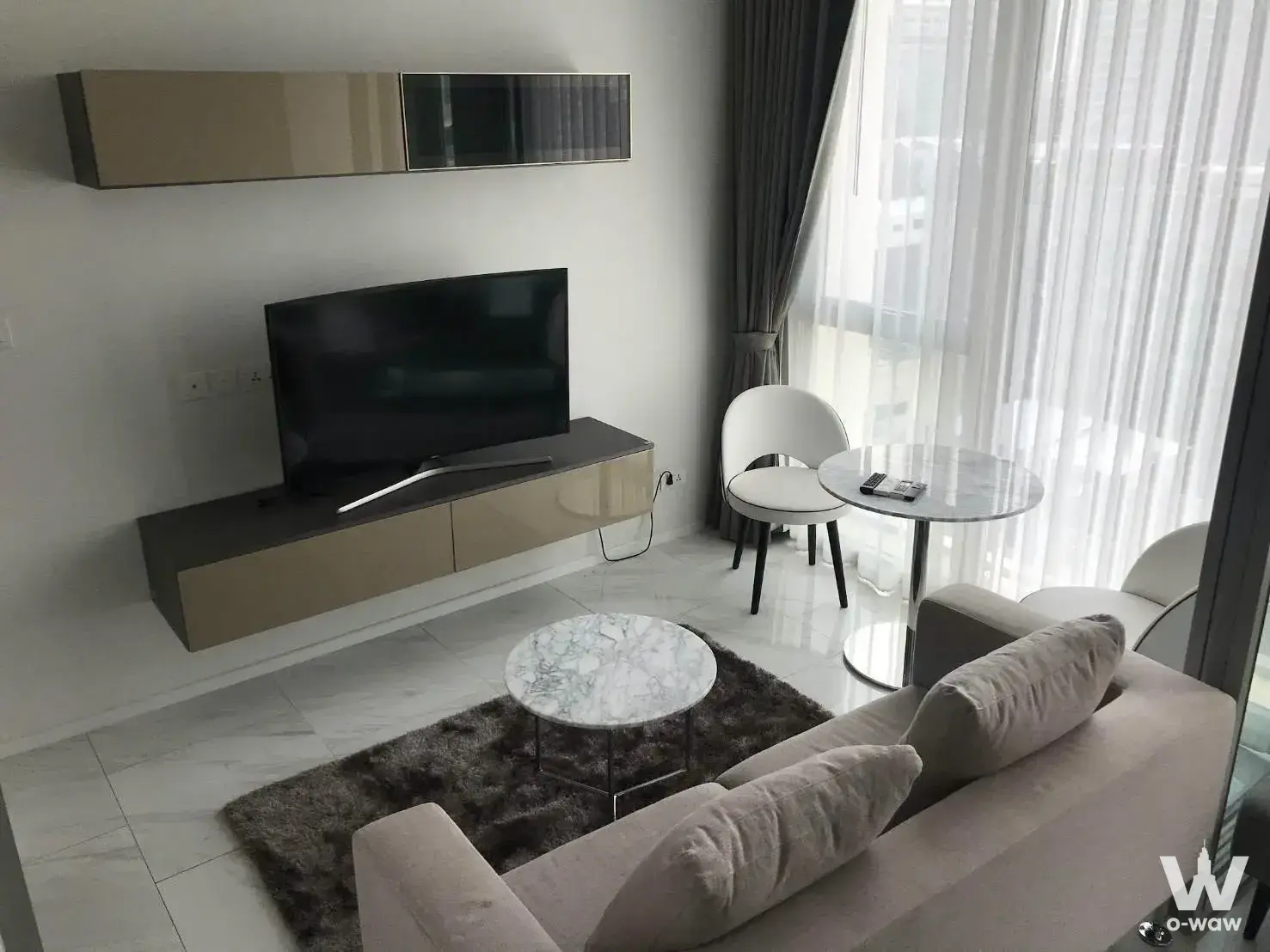Living room with beige sofa, marble coffee table, and city view in HYDE Sukhumvit 11 rental