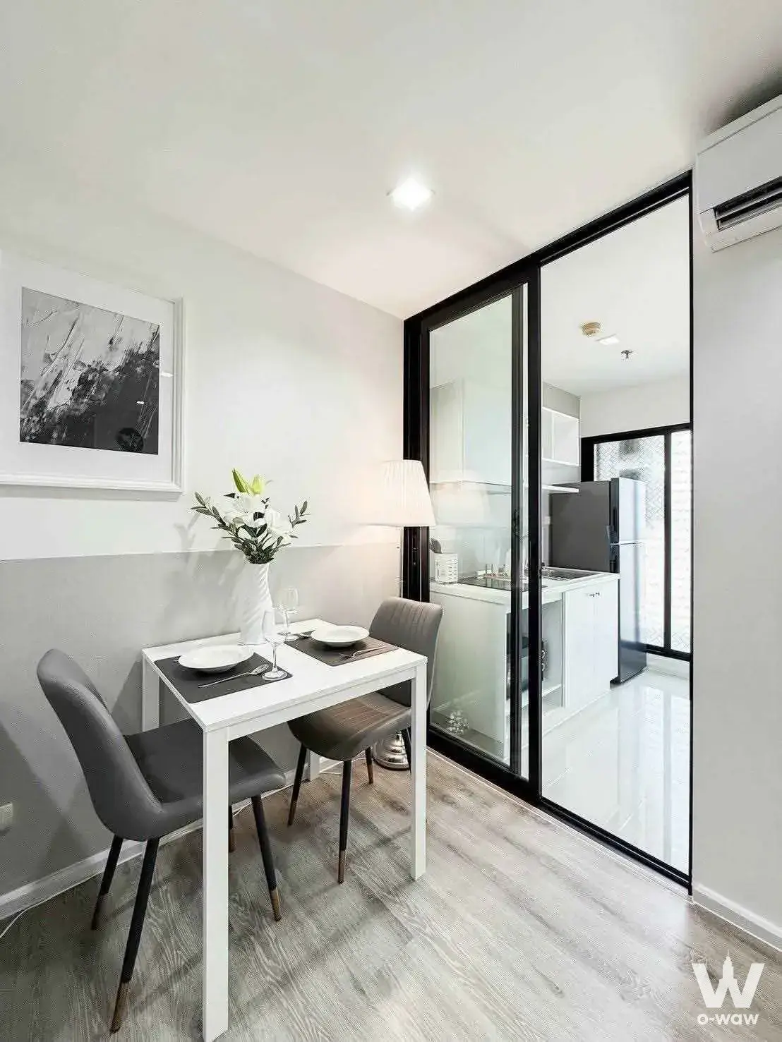 Compact dining space in Knightsbridge Duplex Tiwanon condo with white table set for two and glass-walled kitchen