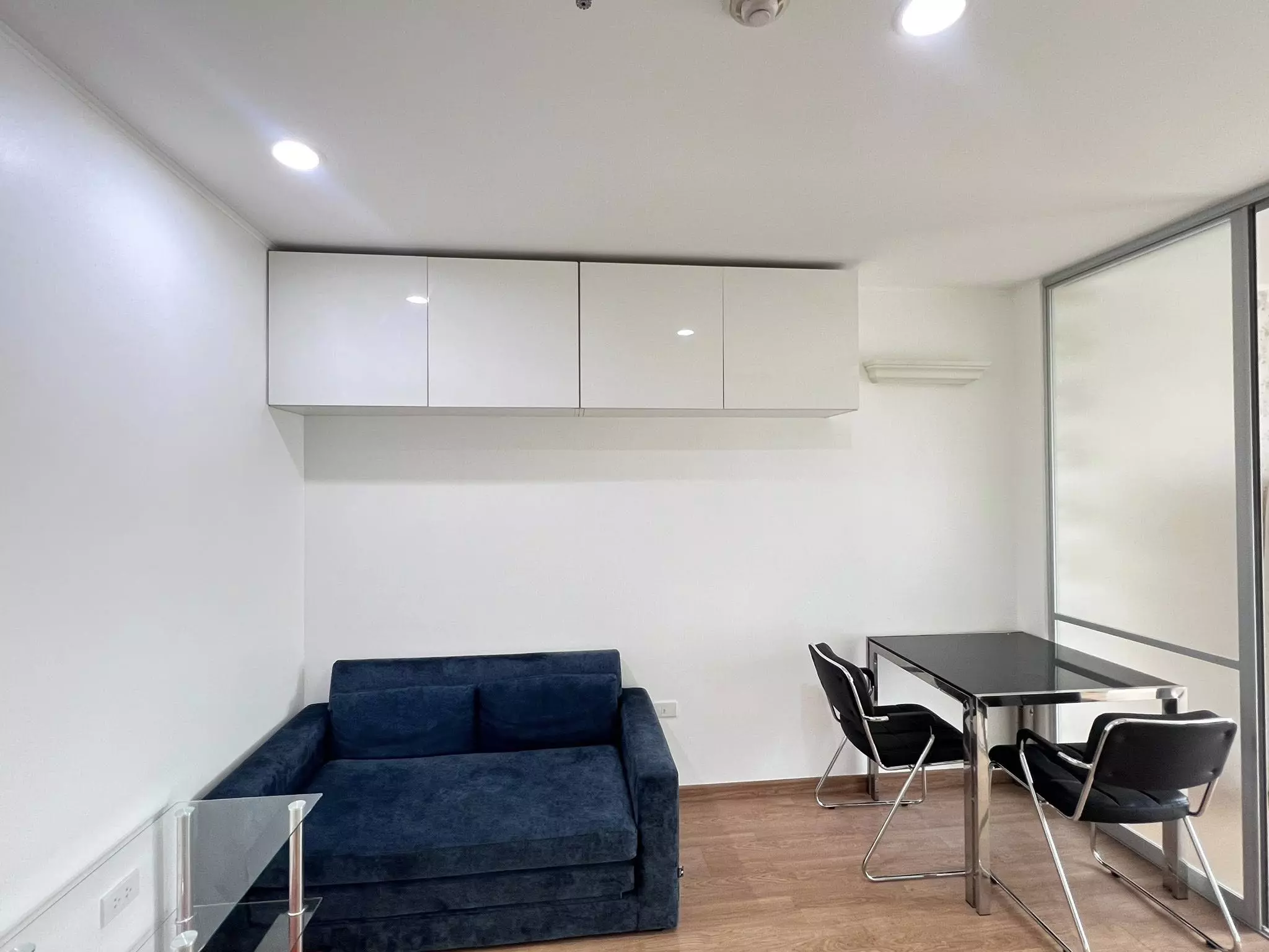 Minimalist studio in U-Delight Jatujak condo featuring navy sofa-bed, wall cabinets, and glass door