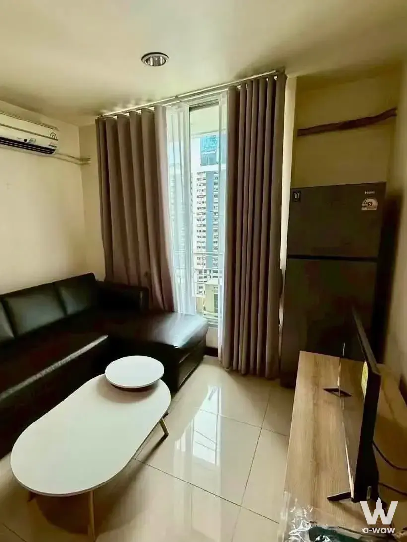 Baan Pathumwan living room featuring brown leather sectional and city view window
