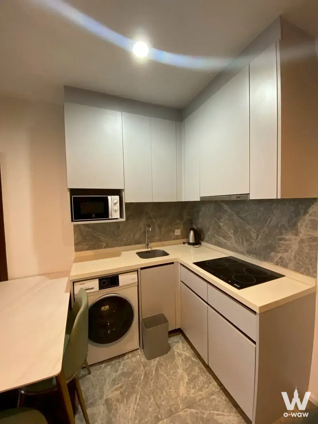 Compact modern kitchen with glossy white cabinets, grey marble backsplash, induction hob, and sage green dining chairs