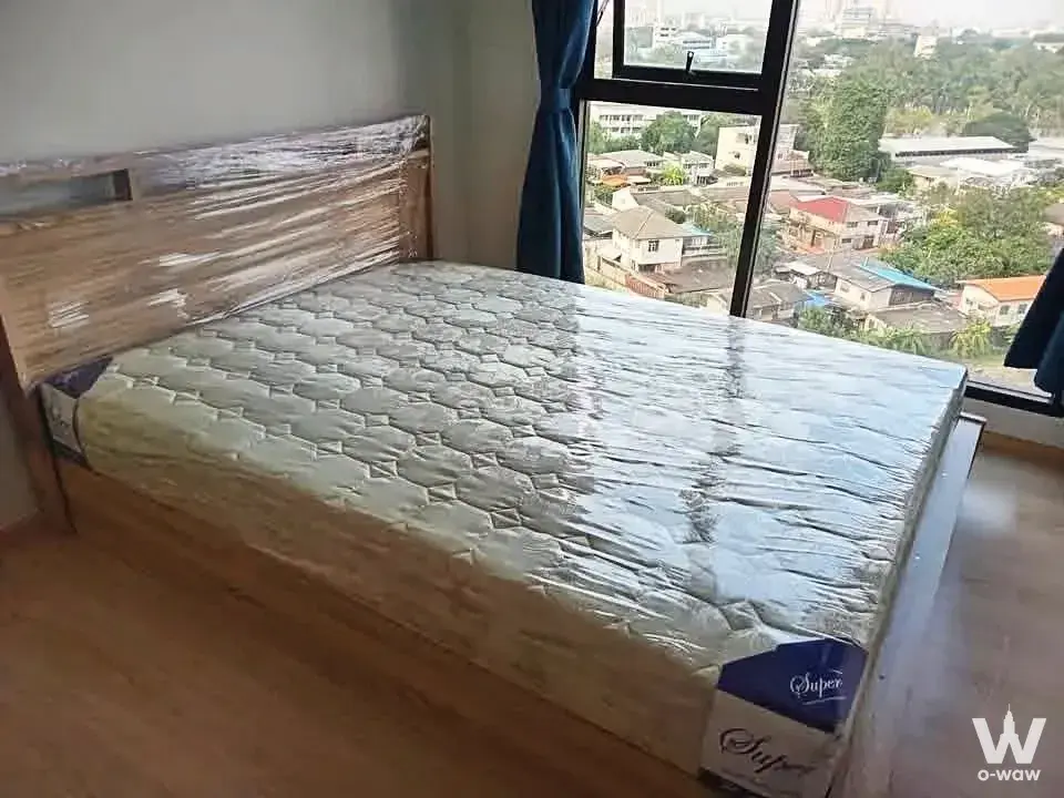 1-bed condo for sale in UNIO H TIWANON with wooden bed frame, plastic-wrapped mattress, and city view