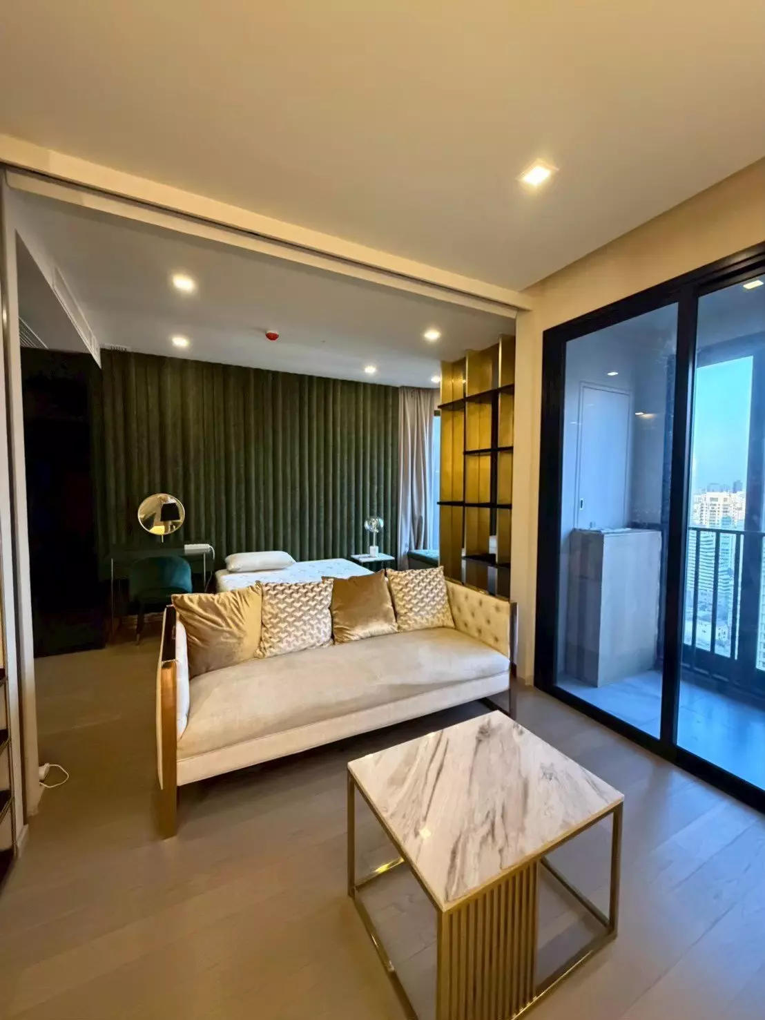 Open-plan studio in Ashton Asoke with velvet sofa, marble coffee table, and city view balcony