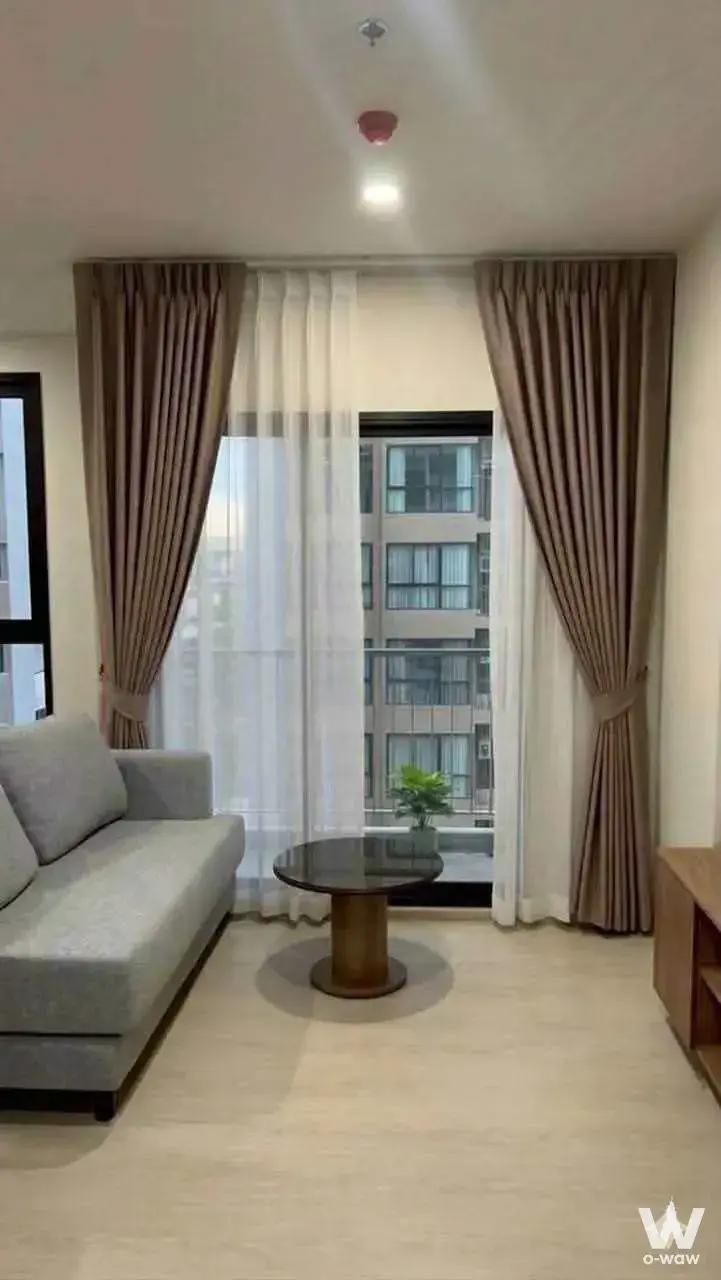 Living room in a 1-bed condo for rent at Nue Riverest Ratburana featuring grey sofa and large windows with balcony access