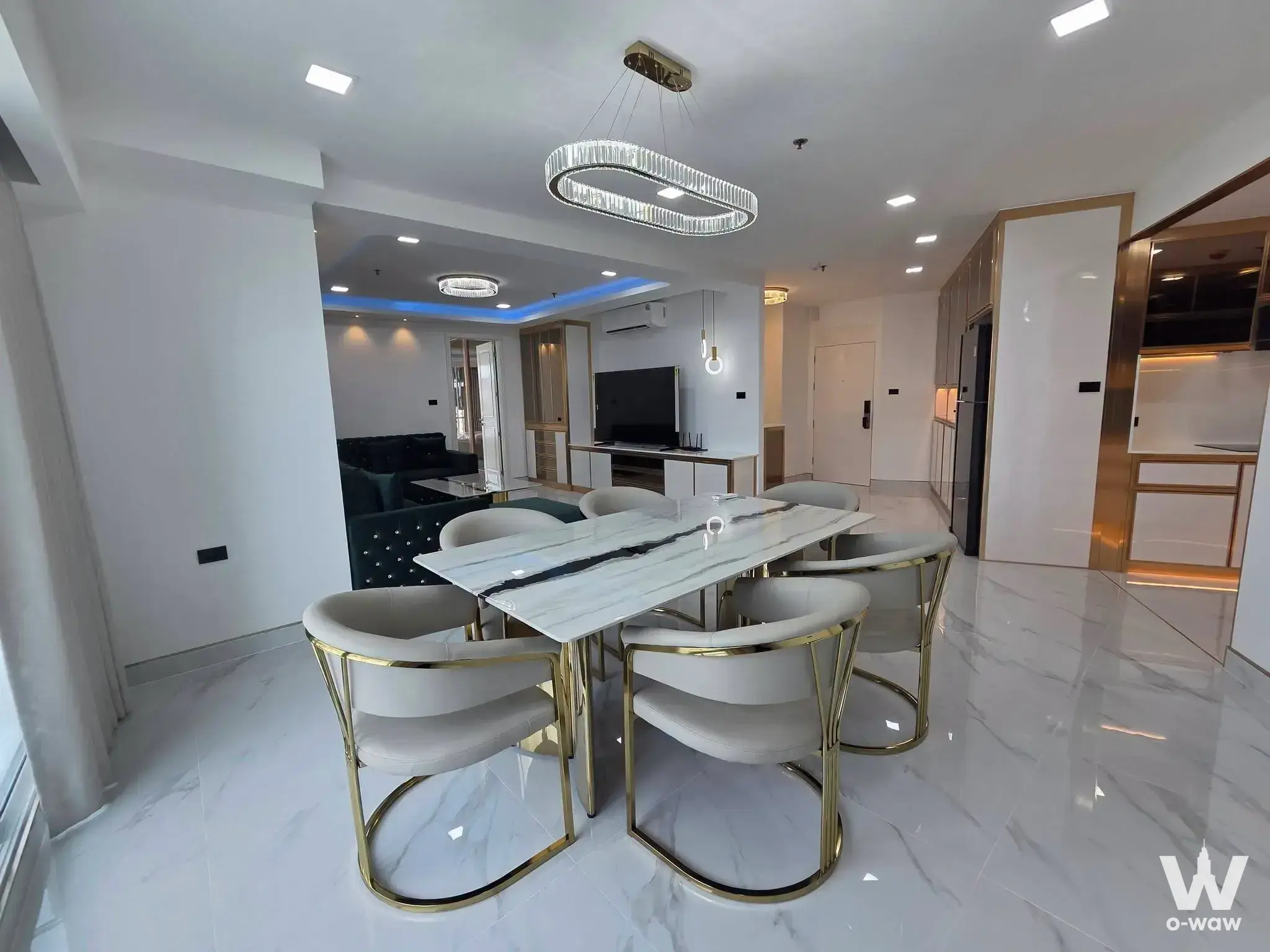 Elegant dining area in Supalai Prima Riva with marble table, gold chairs, and teal velvet sofa in background