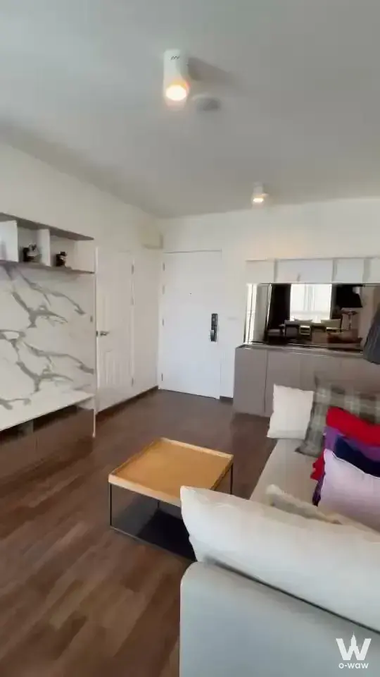 Living area in a U Delight Rachavibha 2-bed condo with grey sofa, marble media wall, and open kitchenette