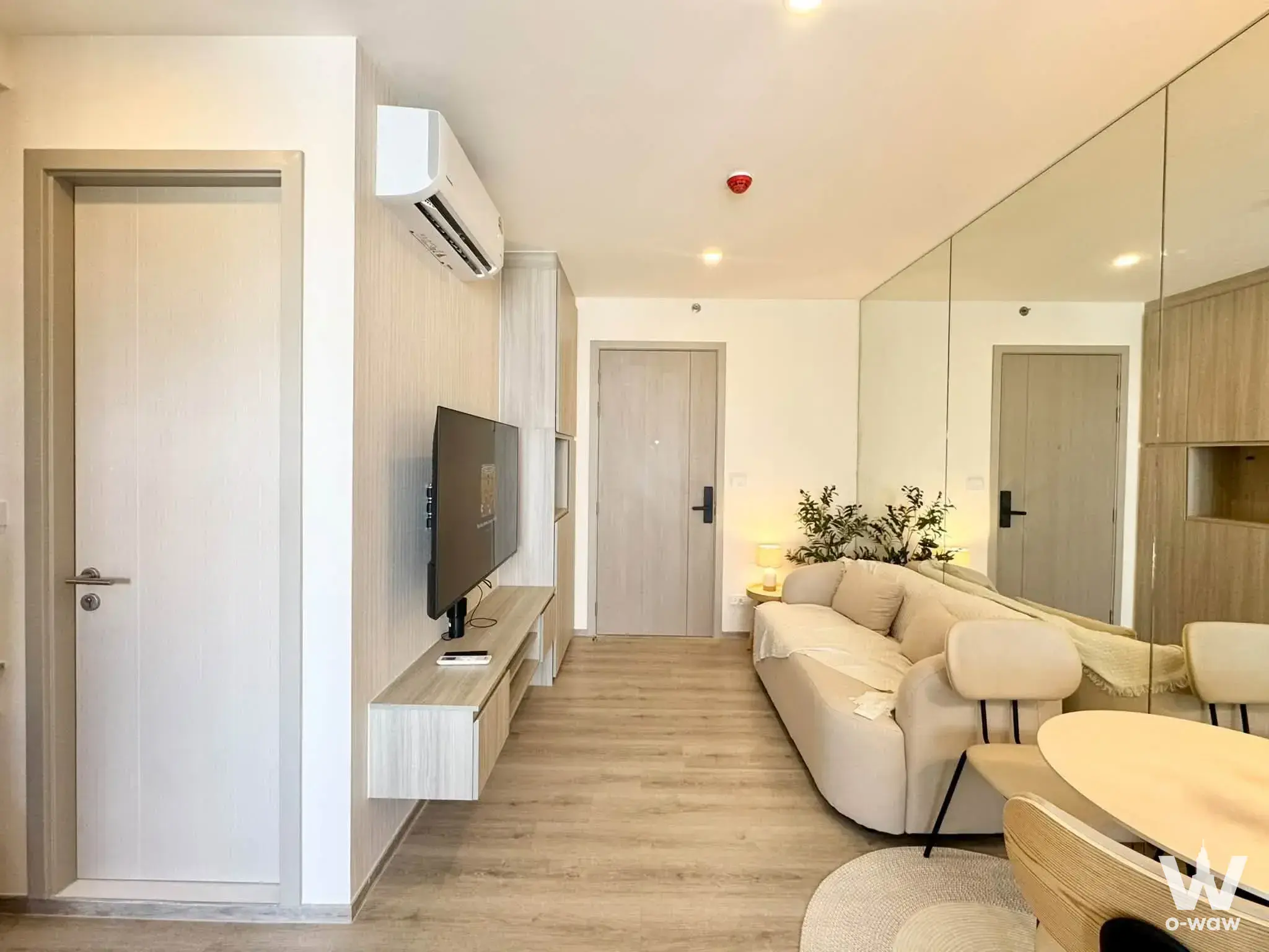 1-bed condo for rent in Origin Place Bangna featuring a living room with light-grey wood flooring and a curved cream sofa