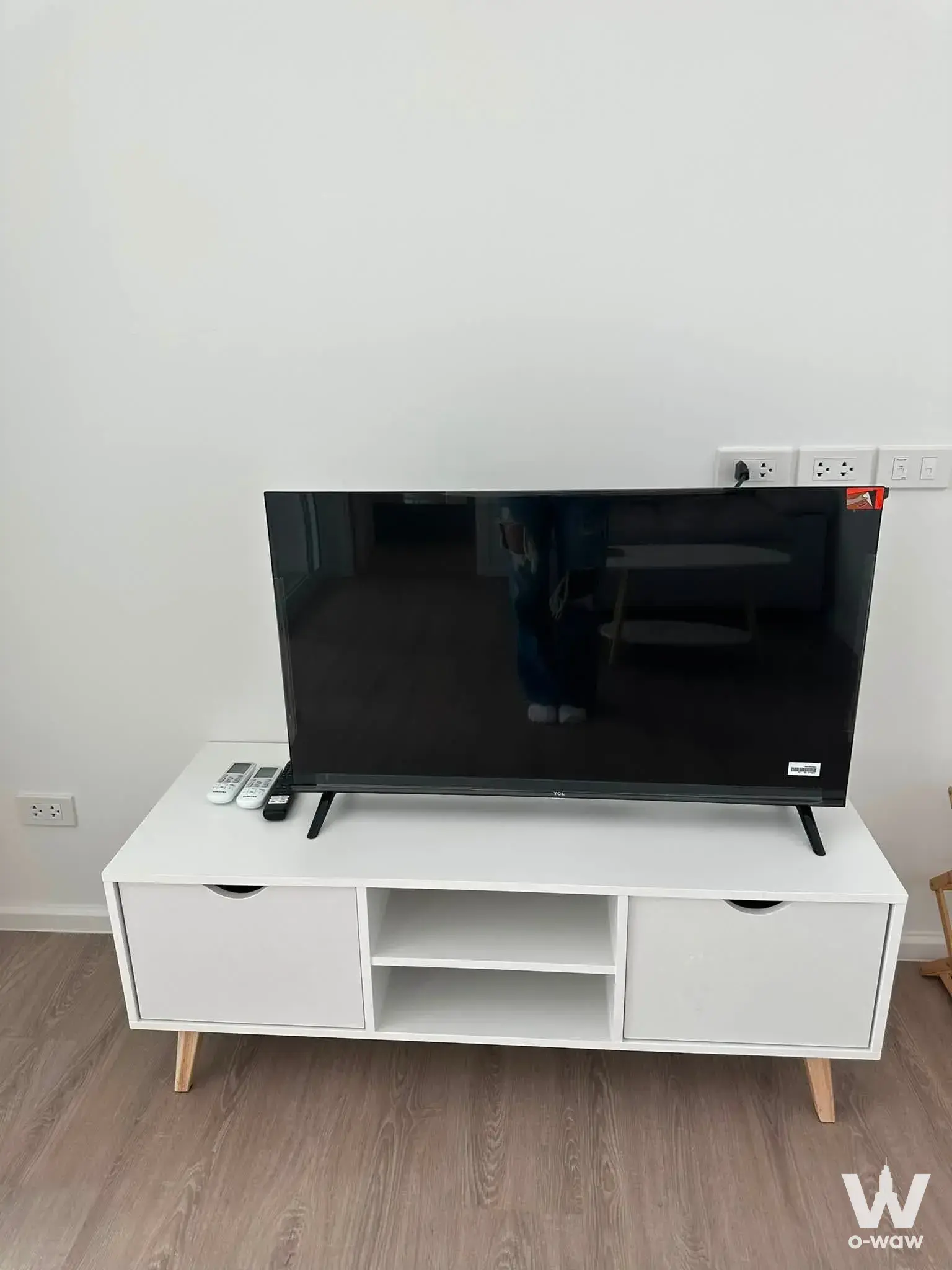 Minimalist living room in Chateau In Town condo with white media console, TV, and light wood laminate flooring