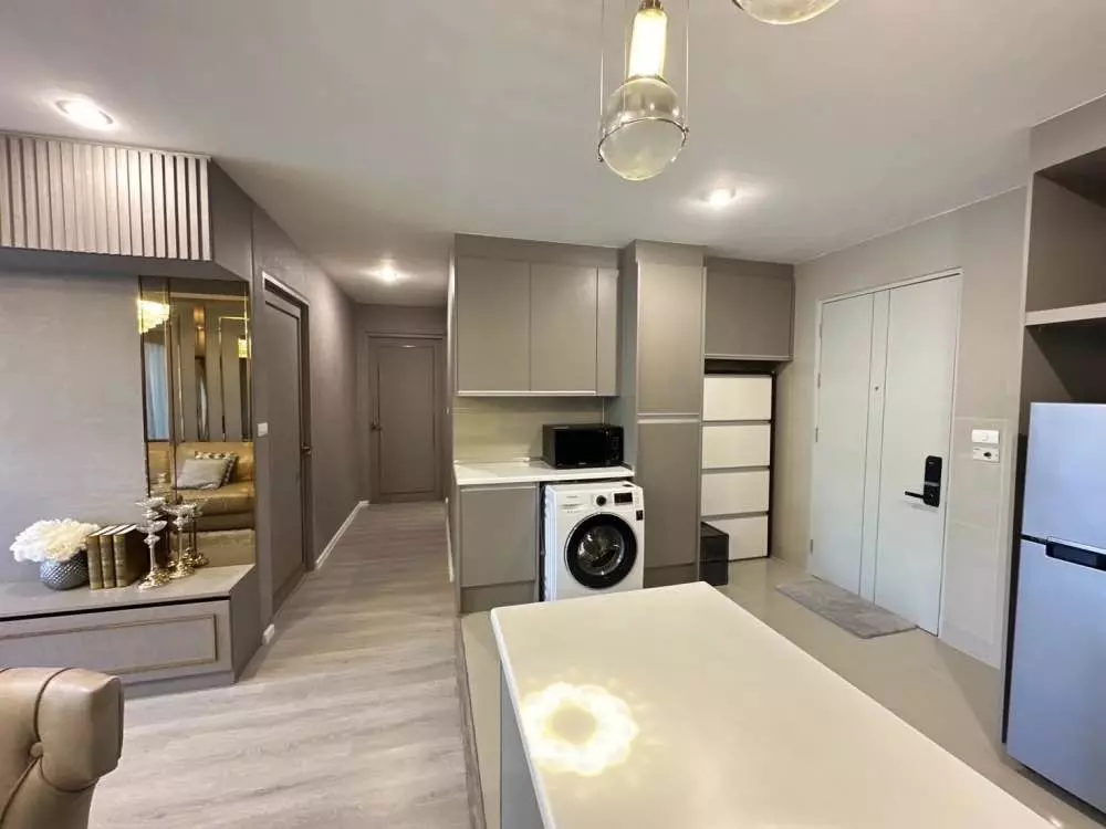 Open-plan kitchen with grey cabinets, island counter, and washing machine in Happy Condo Ladprao