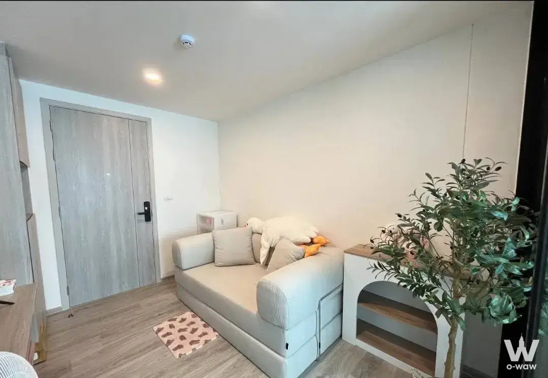 Compact living area in Origin Play Sri Udon with beige sofa, pink paw-print rug, and smart lock door