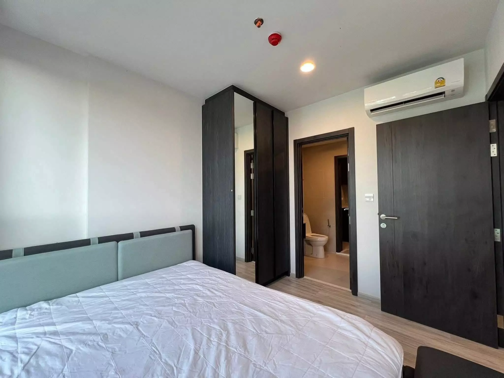 Minimalist bedroom in XT Huai Khwang condo with sage green bed and dark wood wardrobe