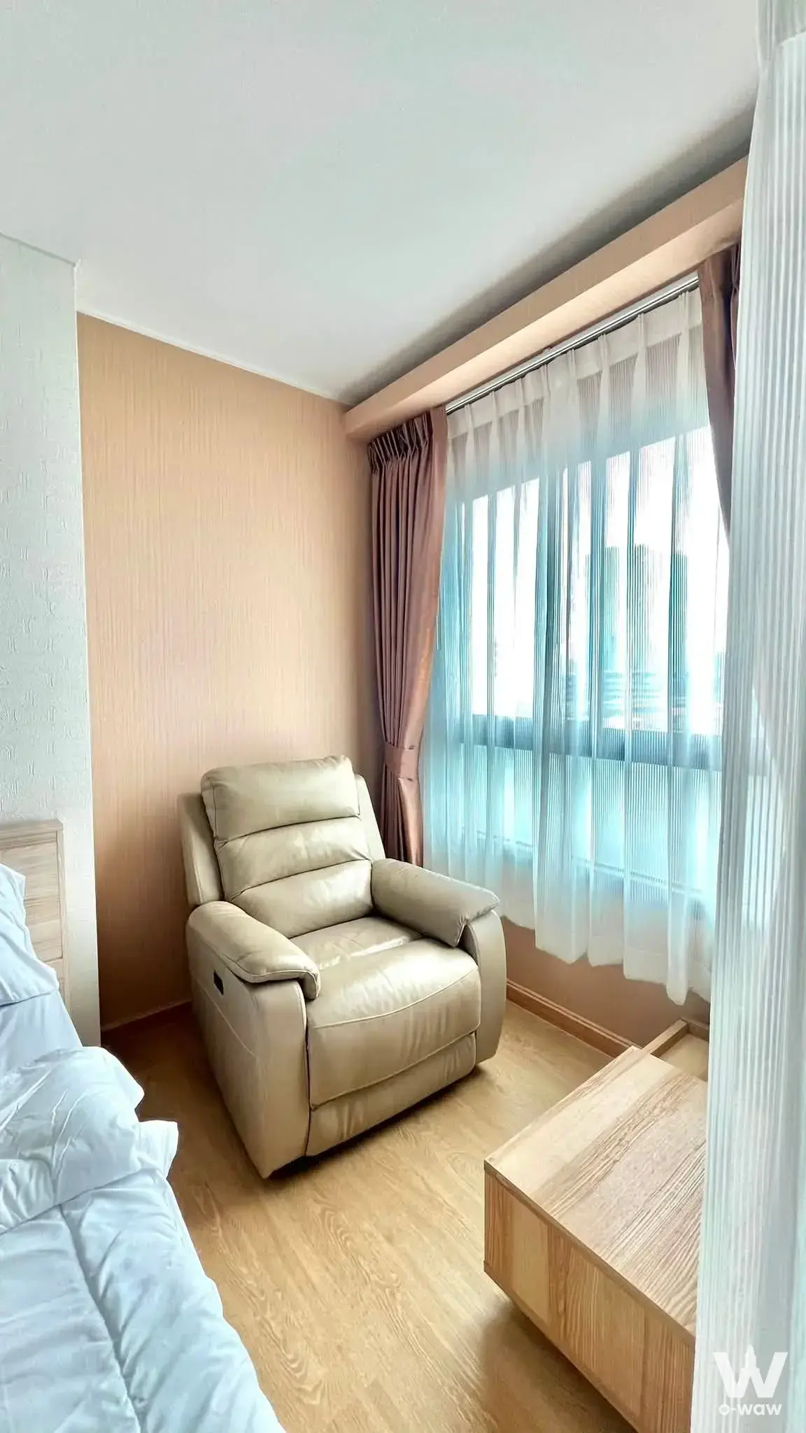 Minimalist bedroom with cream leather recliner, oak flooring, and large window with mauve drapes