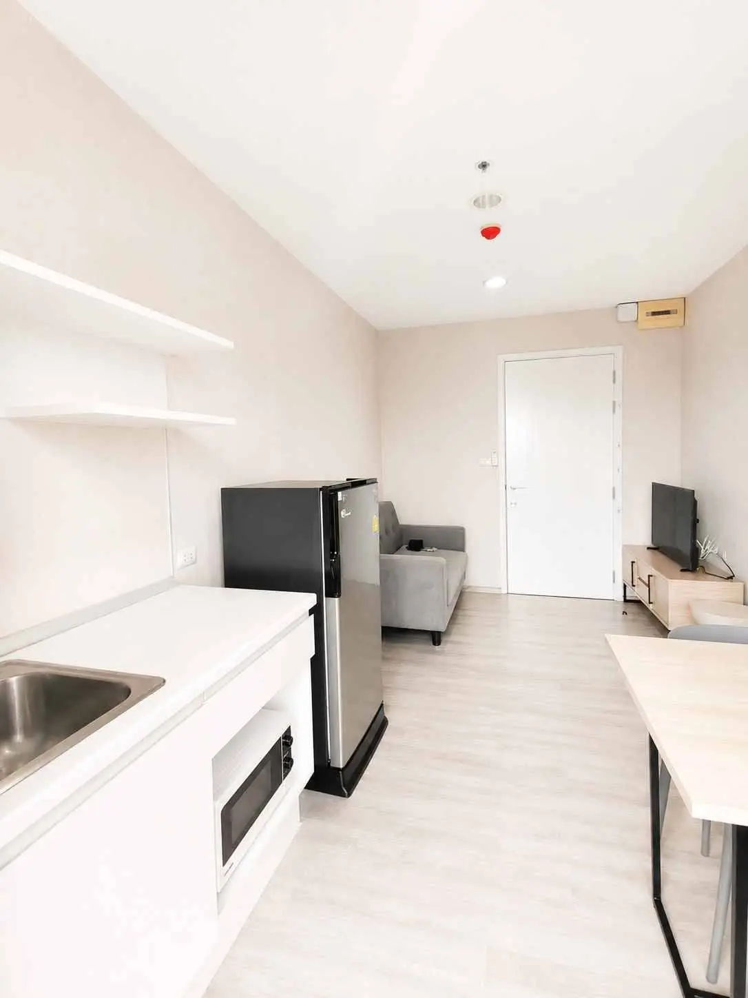 Open-plan studio at Plum Condo Central Station featuring a sofa, dining table, and compact kitchenette