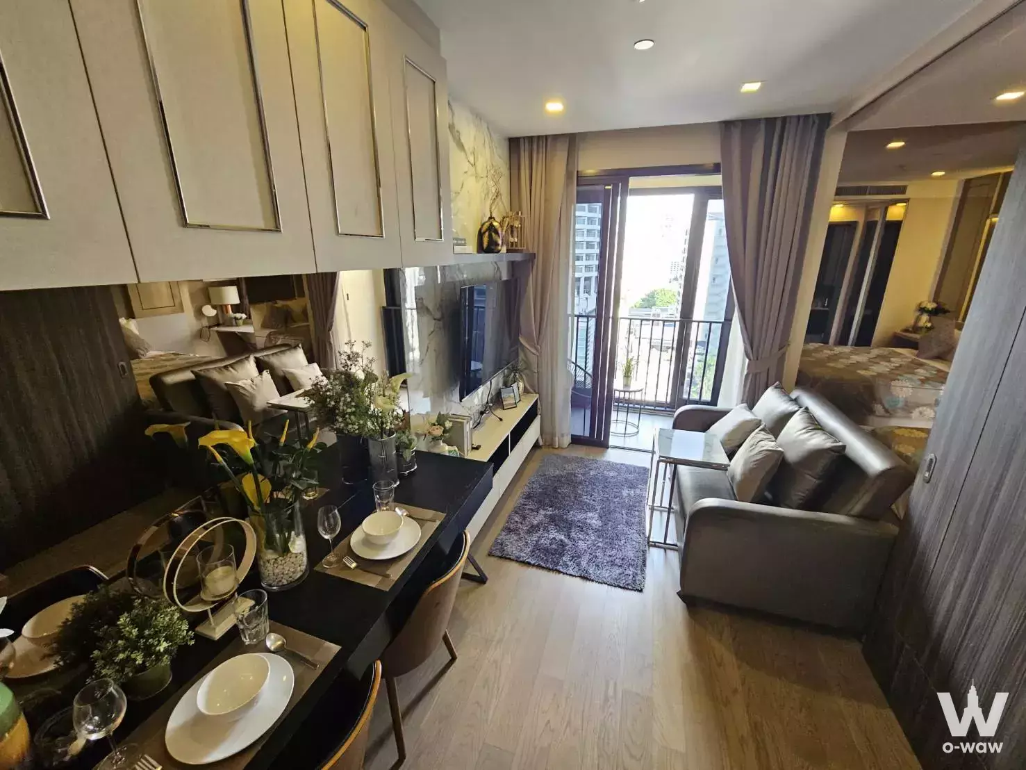 Ashton Asoke studio with dining set, gray leather sofa, purple rug, and balcony access to city views