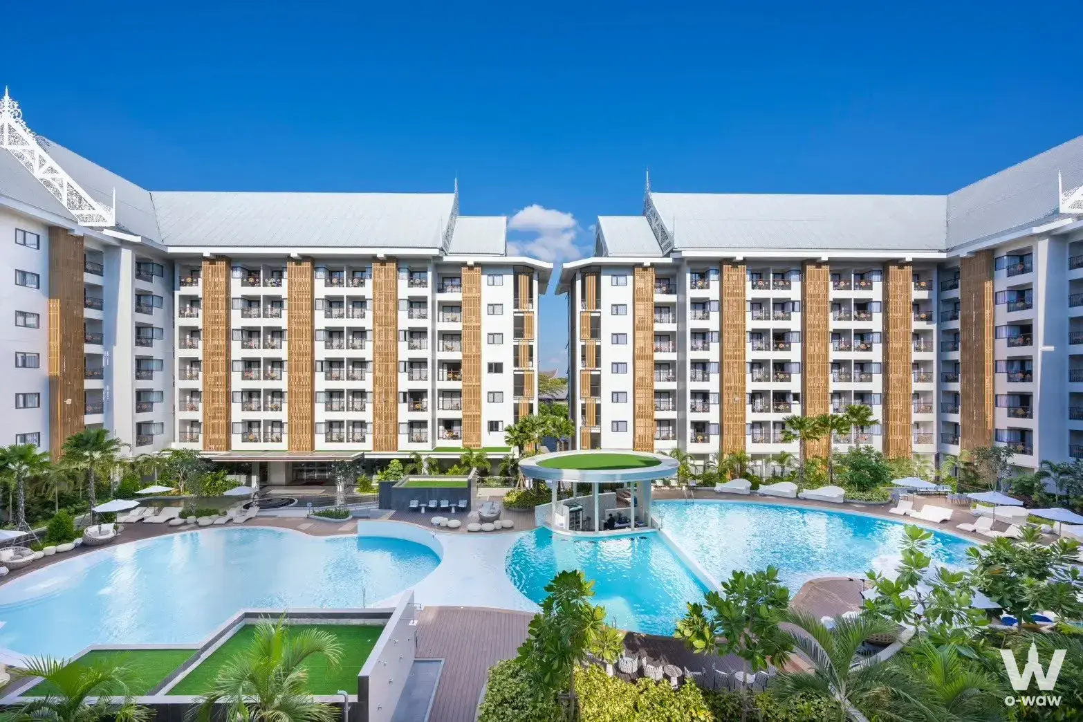 Exterior of Wyndham Jomtien Pattaya condo for sale showing resort-style pool, white buildings, wooden slats, and tropical