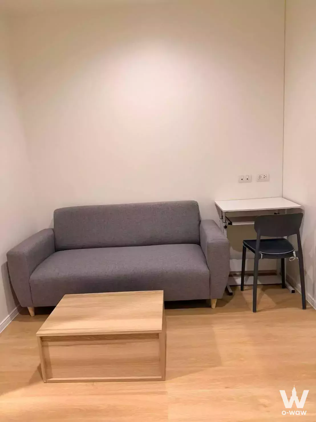 Compact living area with grey sofa, oak coffee table, and corner desk in Lumpini Park Phetkasem 98 condo