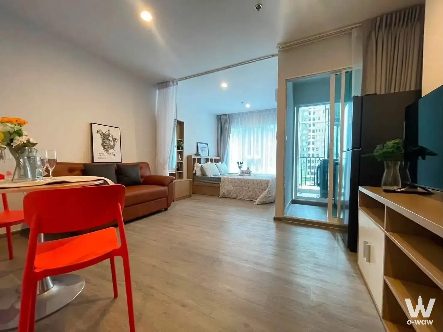 Furnished studio condo at Regent Home Bangna with brown leather sofa, glass dining table, and balcony access