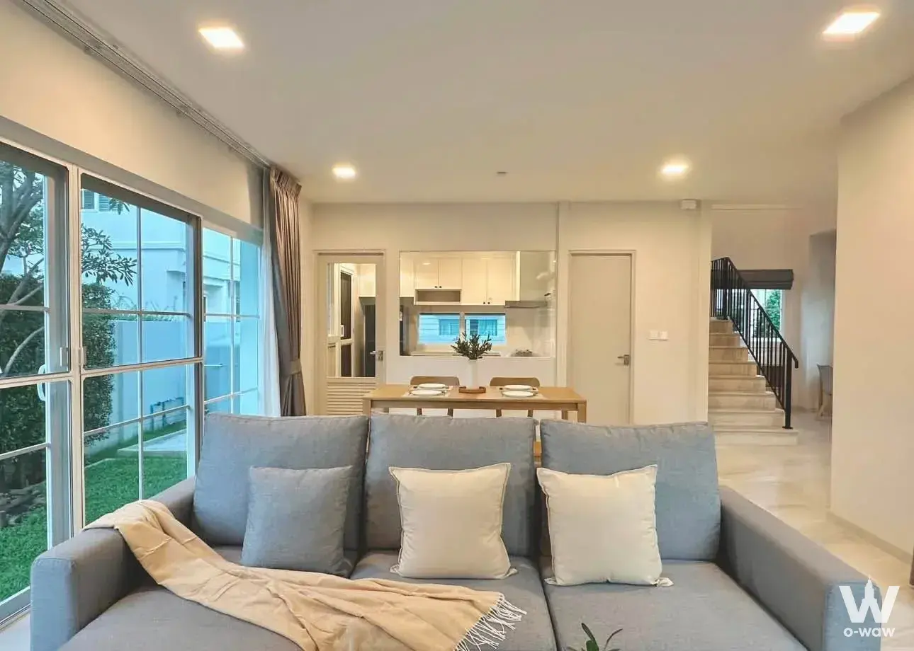 Living room has grey sofa, sliding glass windows and open kitchen in a 3-bed rental in Chaiyapruek Bangna KM.15