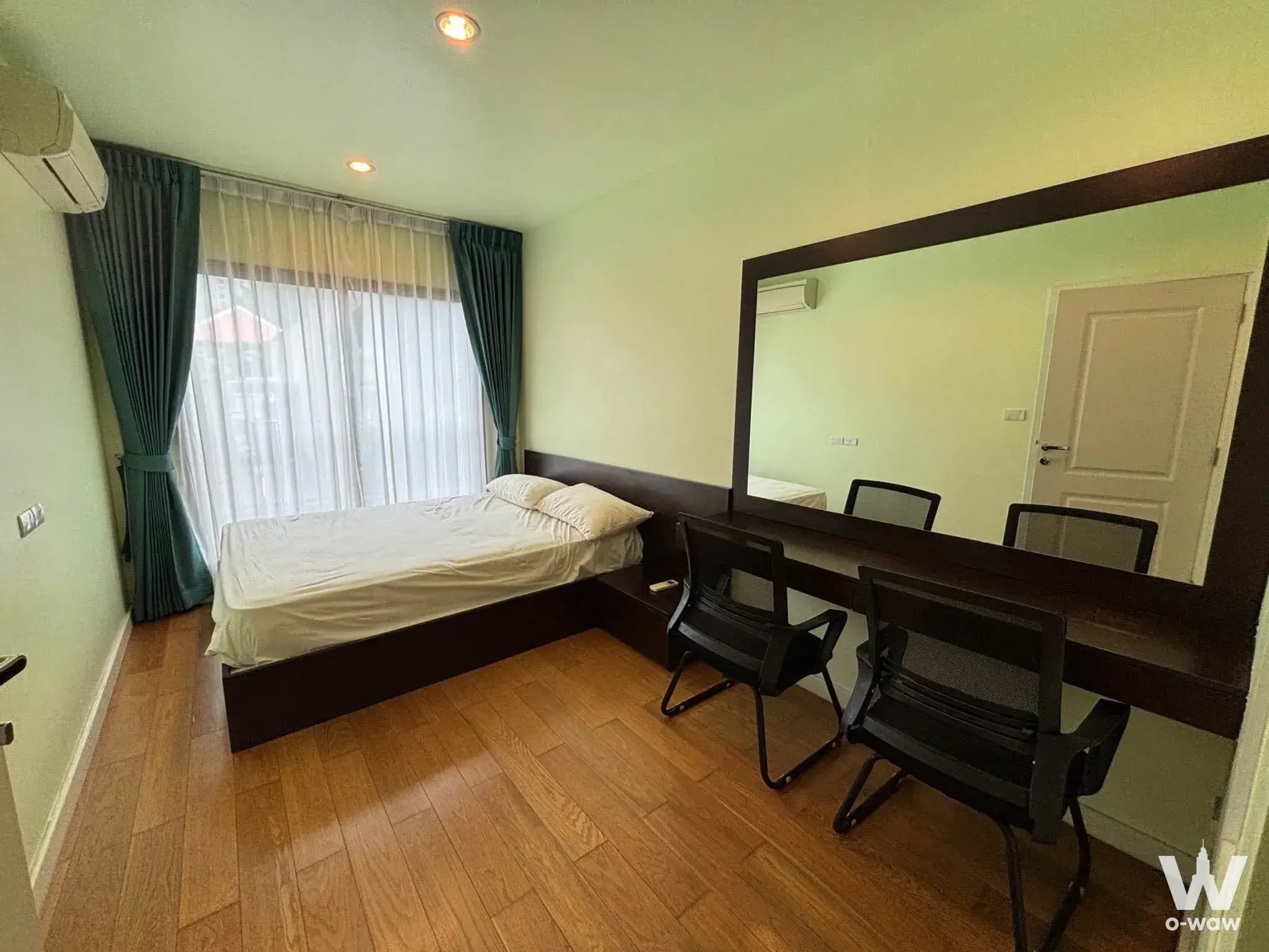 Compact bedroom in Condolette Dwell with dark wood desk, large mirror, teal curtains, and mint-green walls