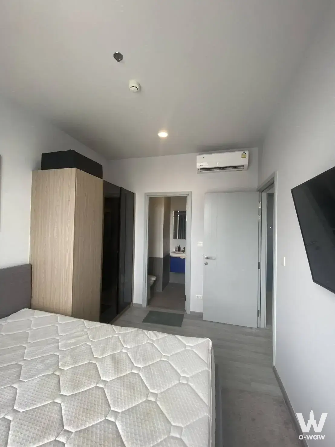 Minimalist bedroom with grey upholstered bed and oak wardrobe in XT Ekkamai 1-bed condo for rent