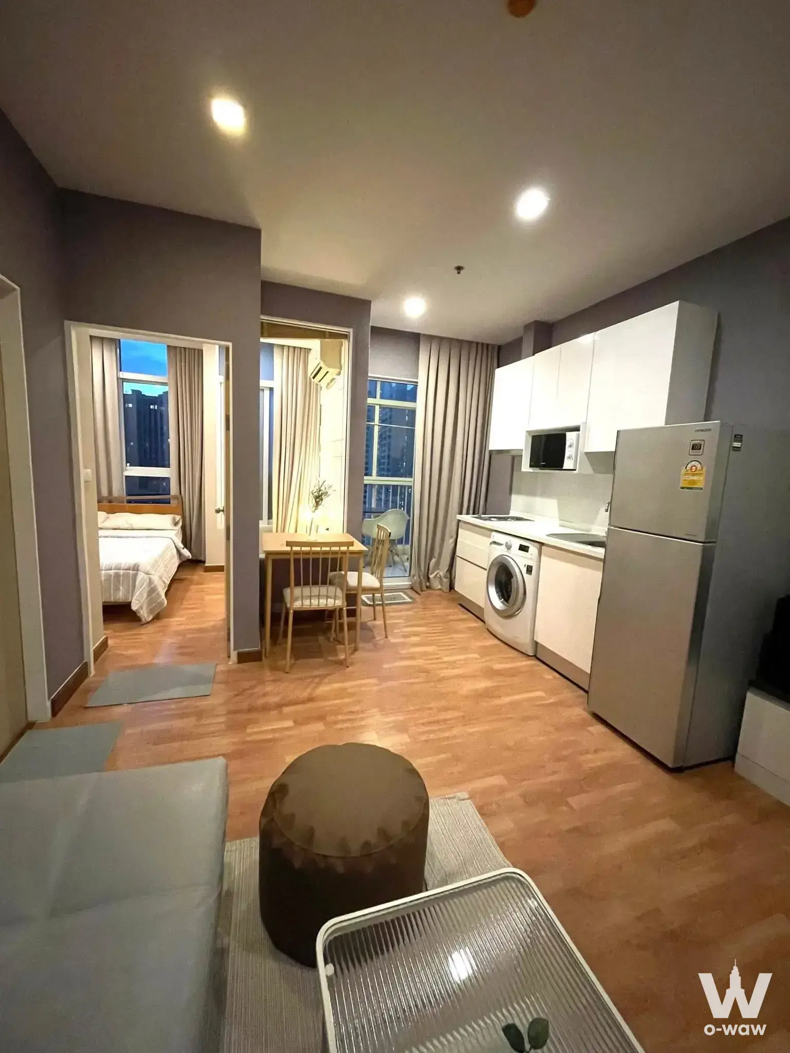 Open-plan 1-bed condo for rent in The Coast Bangkok with wood floors, grey sofa, and kitchenette