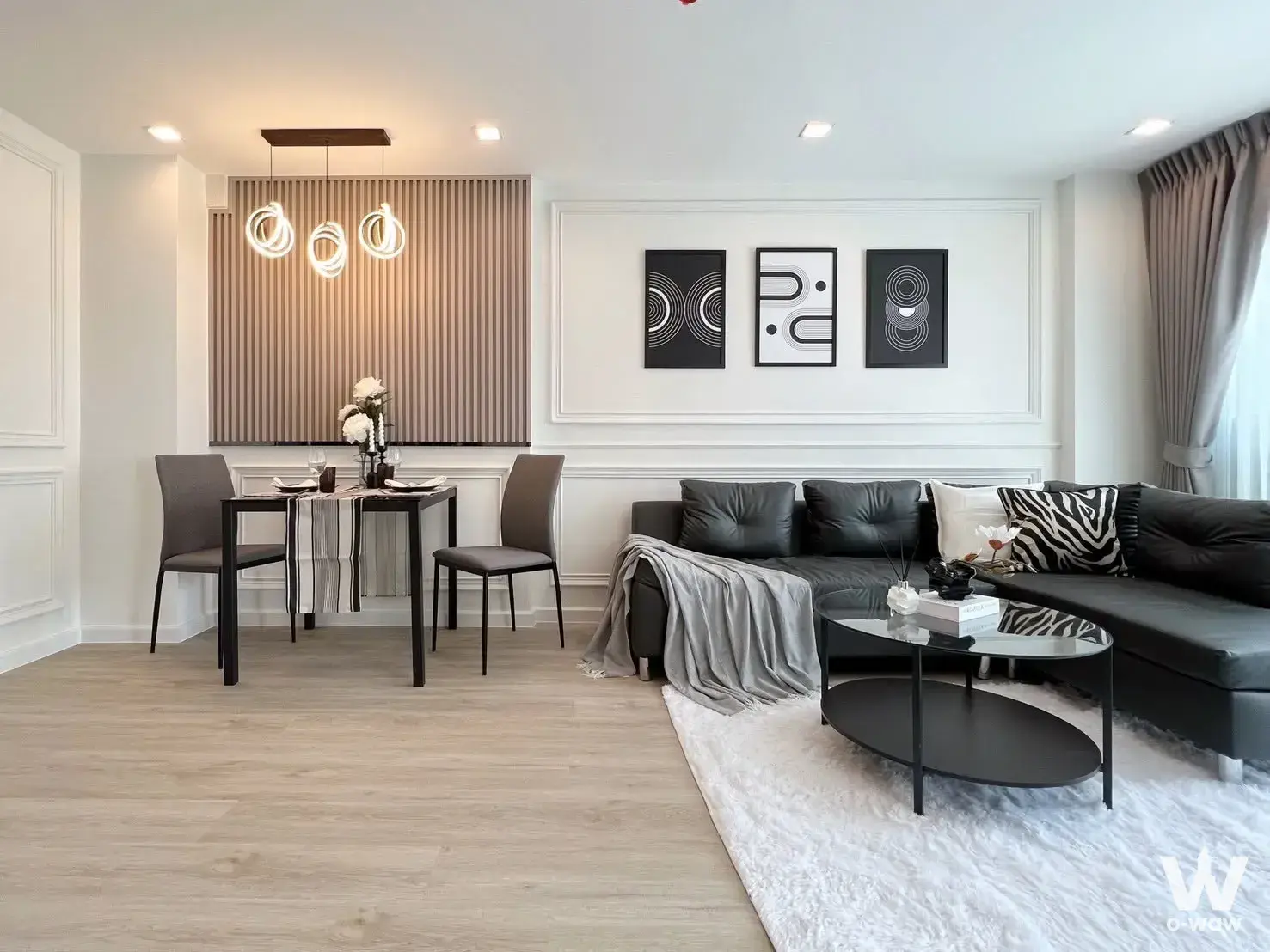 Luxury open-plan living space in Casa Condo Sukhumvit 97 with a black leather sectional and vertical wood slat accent wall