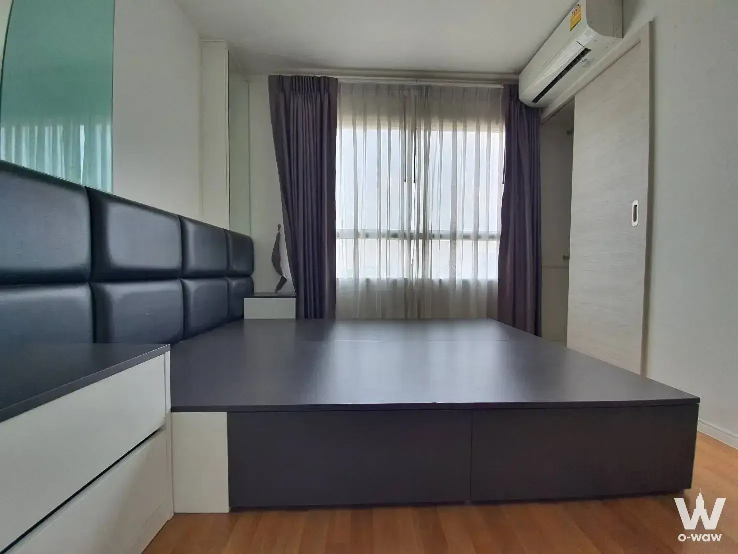 Empty bedroom with grey padded headboard and honey-brown laminate floors in a Lumpini Park Rama 9 condo for sale