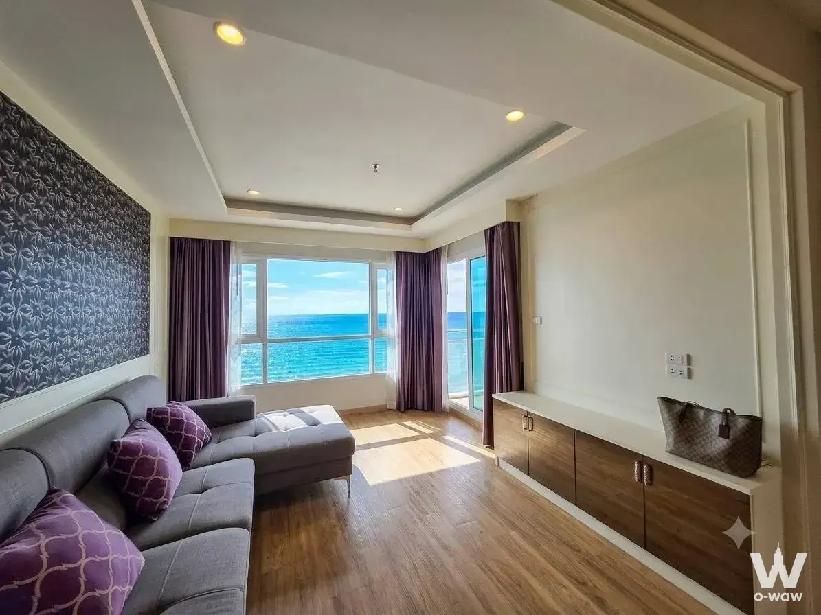 Living room with grey sectional sofa and ocean view through purple curtains in The Zea Sriracha condo