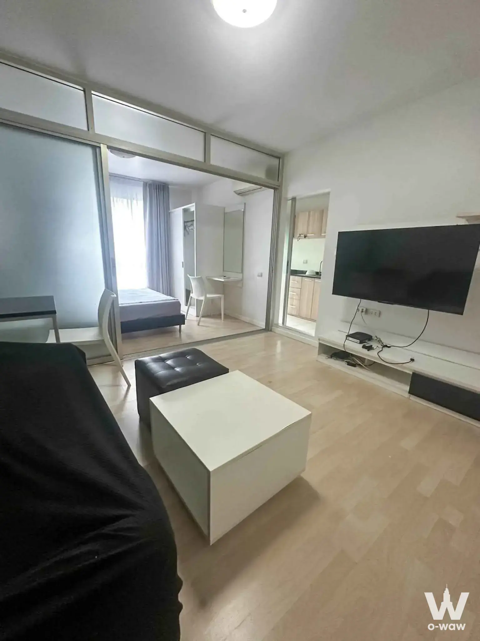 Dcondo Ramkhamhaeng 64 1-bed condo living room with black sofa and glass partition to bedroom