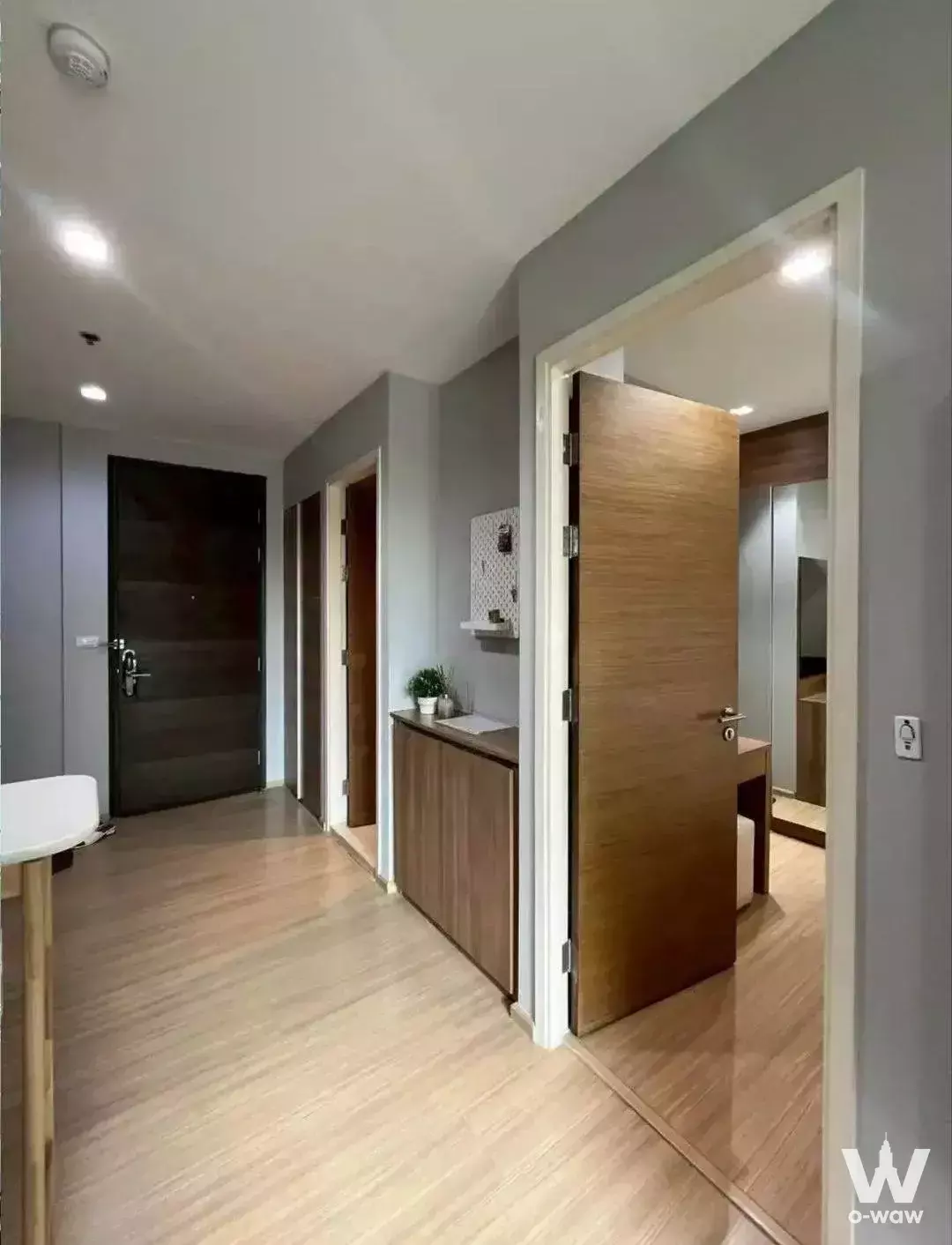 Entry hallway of a 1-bed Rhythm Sukhumvit 50 condo featuring light oak floors, grey walls, and built-in wooden cabinets