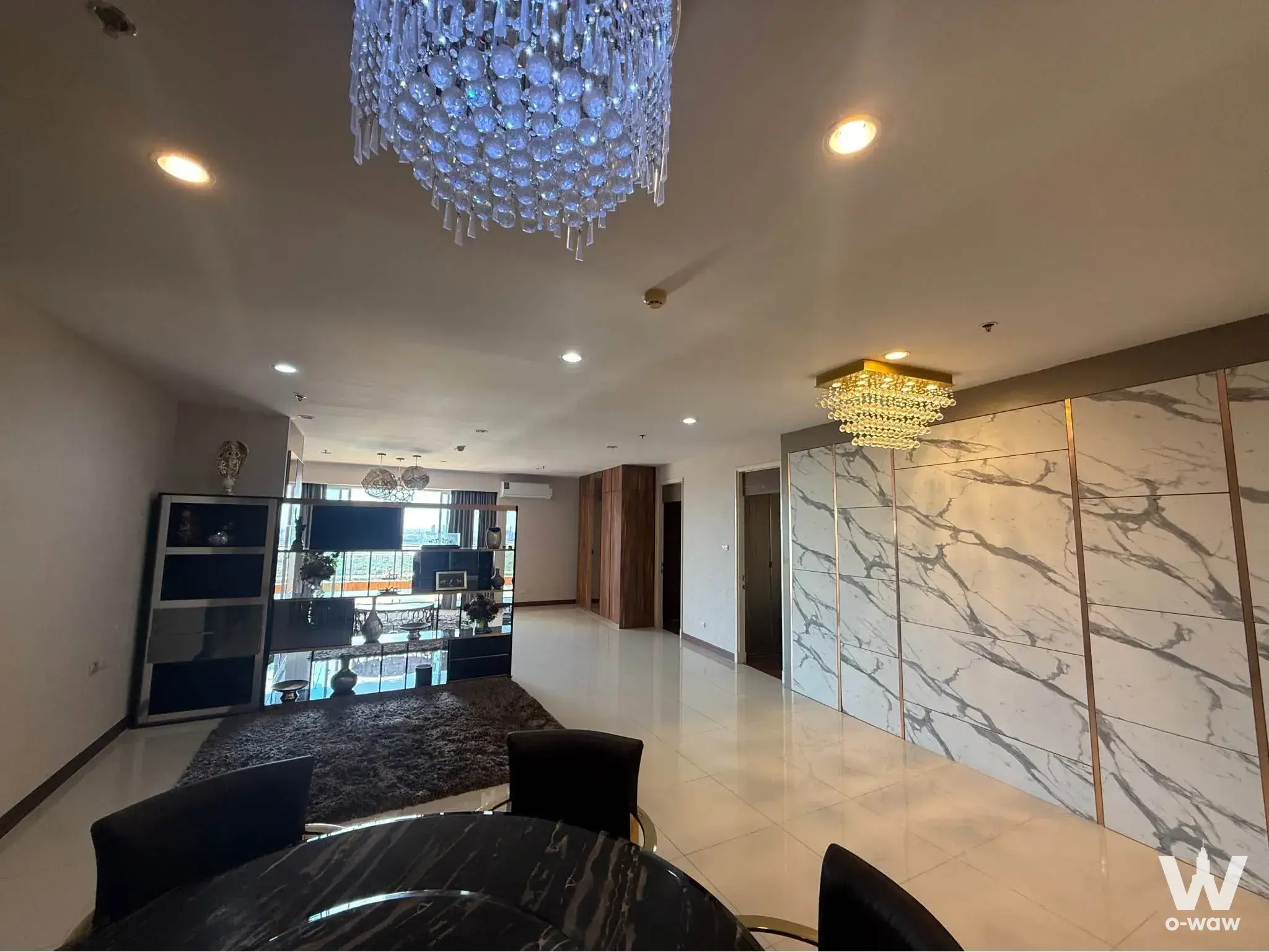 Dining area of this Supalai Prima Riva condo showcases a marble table, crystal chandelier, and floor-to-ceiling windows