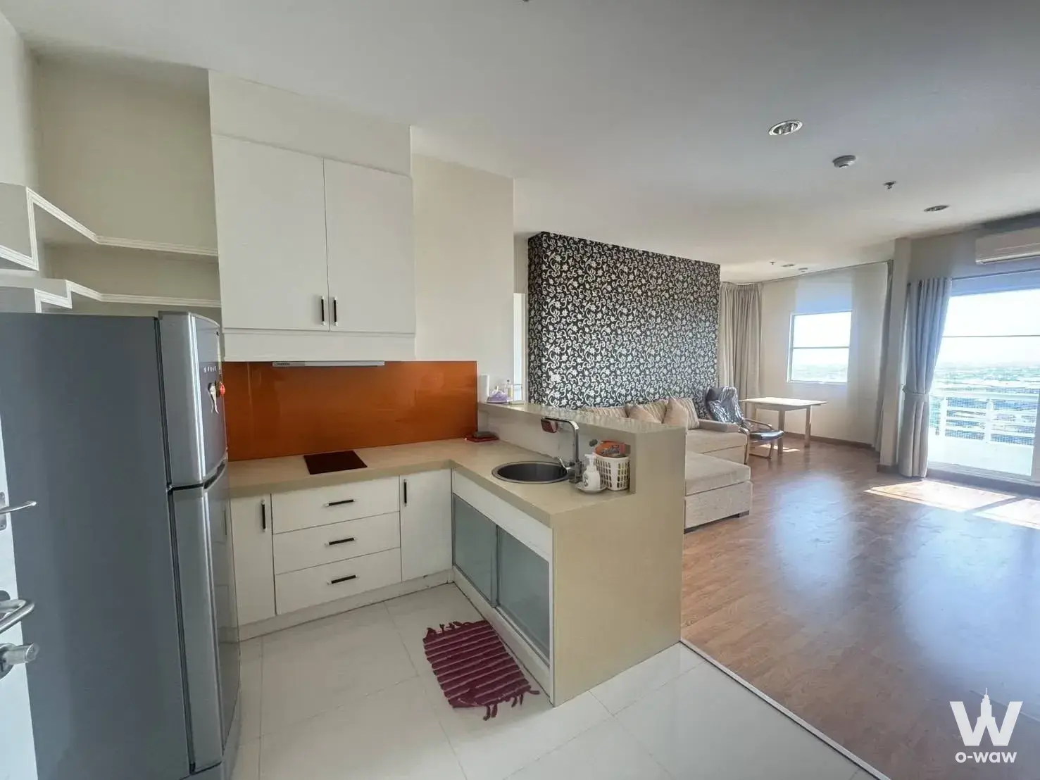 Open-plan kitchen with orange glass backsplash and beige sectional sofa in a 1-bed condo for sale at The Fourwings Residence