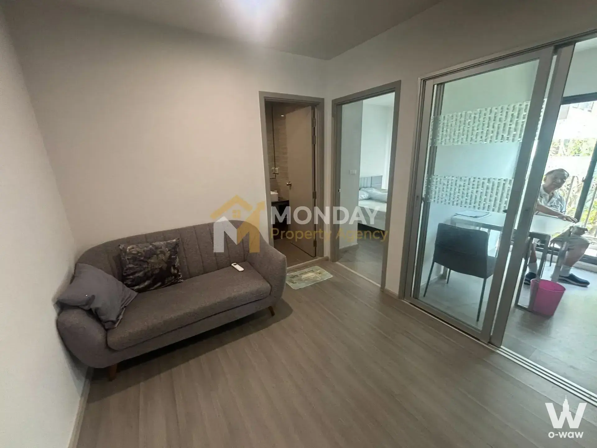 Living room in a The Parkland Charan-Pinklao condo featuring a grey sofa and sliding glass doors leading to a balcony