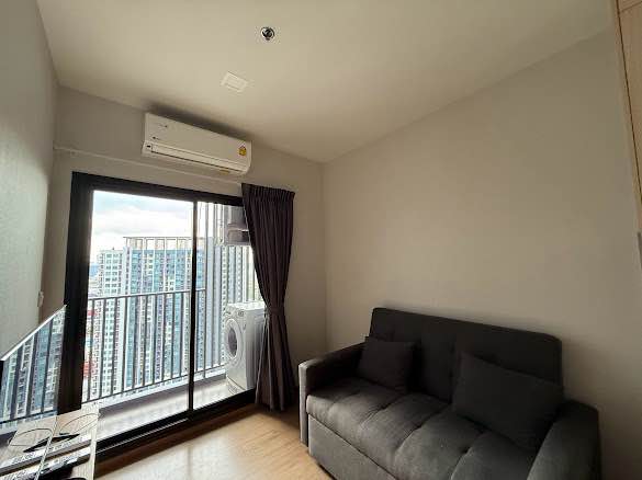 Living room in Metris Rama 9 Ramkumhang 1-bed condo with grey sofa and balcony access