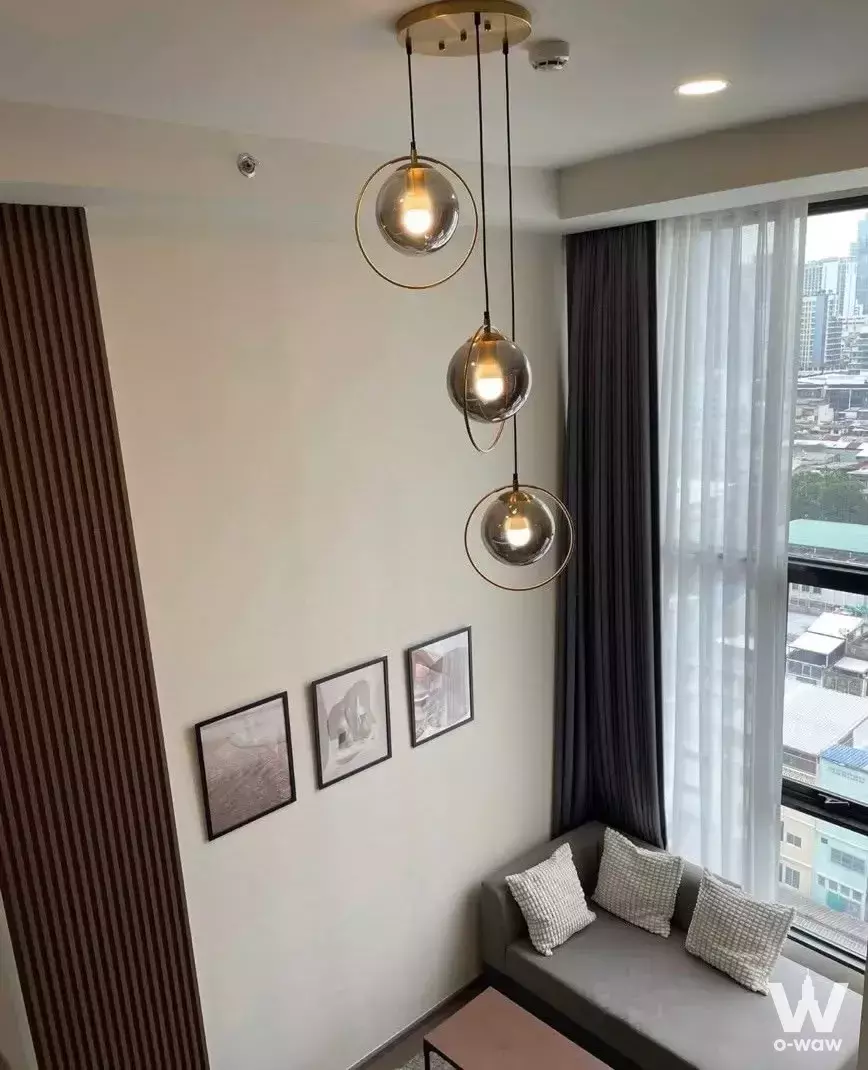 Living corner in Chula-Samyan condo with brass pendant lights, wood slat paneling, and a city view from the window