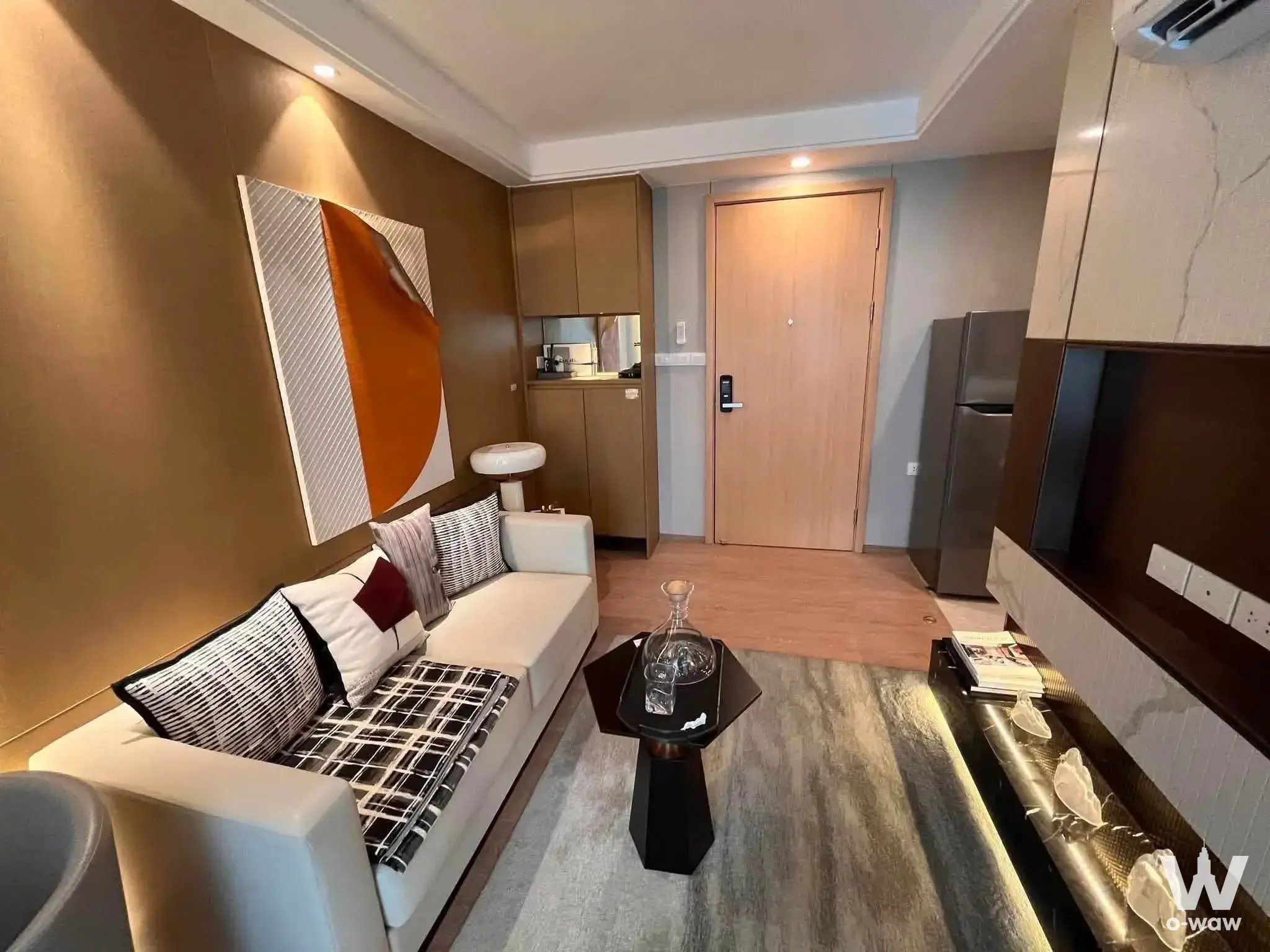 Furnished living room in Regal Srinakarin 40 condo featuring a beige leather sofa, marble side table, and orange accent art