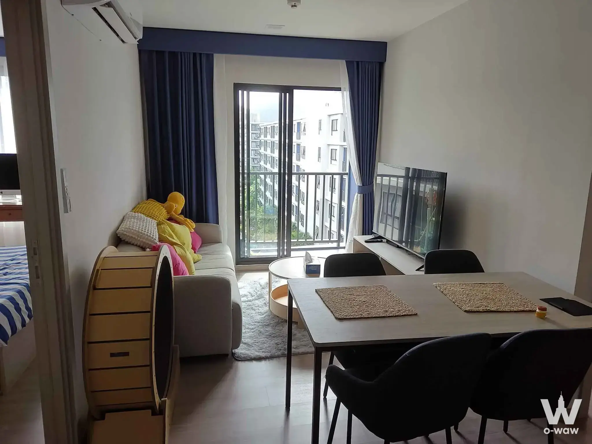 The open-plan living and dining area in this 2-bed Dcondo Reef Phuket condo has a grey sofa and balcony city view