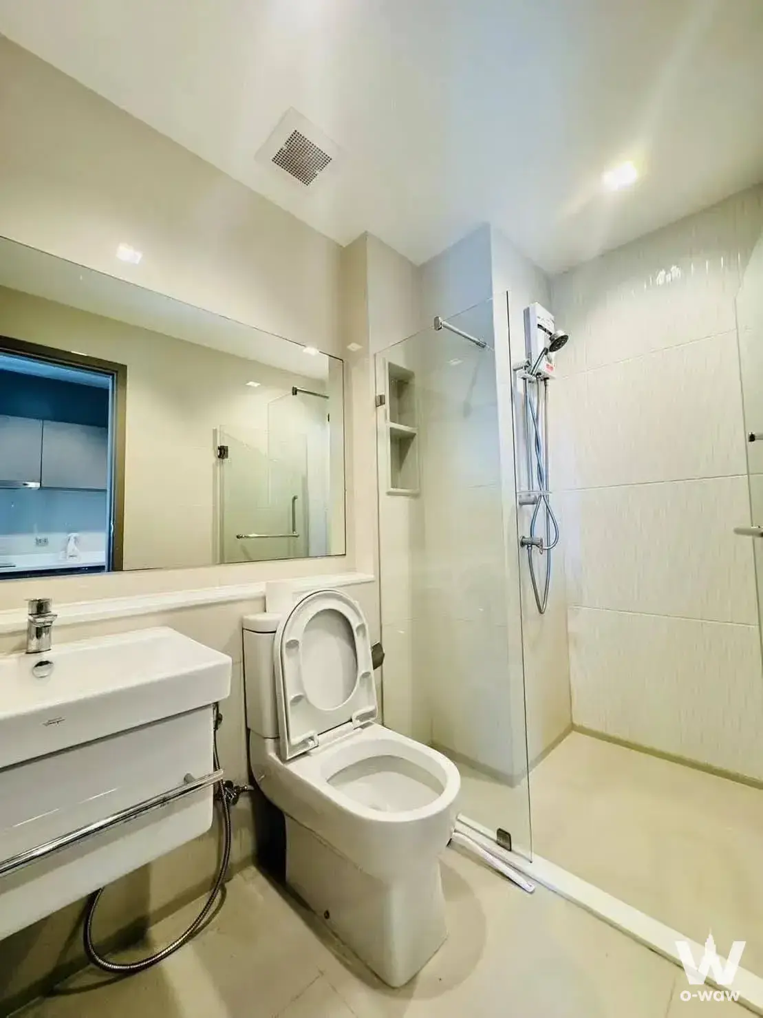 Compact bathroom in a Life Asoke rental featuring white tiles and a walk-in glass shower stall