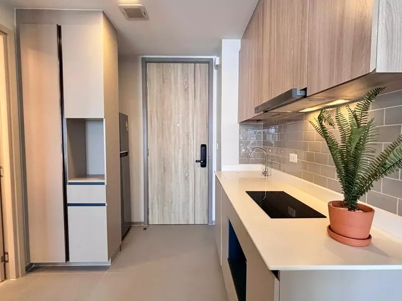 Galley kitchen in a 1-bed XT Phayathai condo with black induction cooktop and oak cabinets