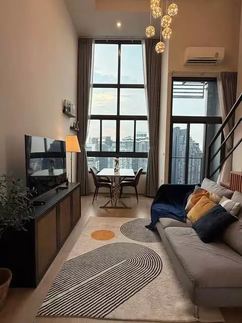 Living area in an IDEO Rama 9 Asoke condo with a grey sofa, dining nook, and high-floor city skyline views