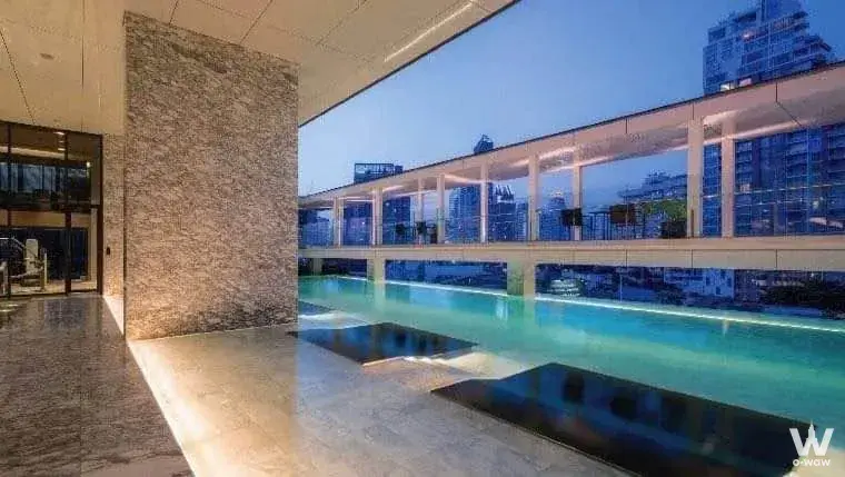 Rooftop infinity pool at BEATNIQ offers turquoise water and city skyline views against beige stone decking