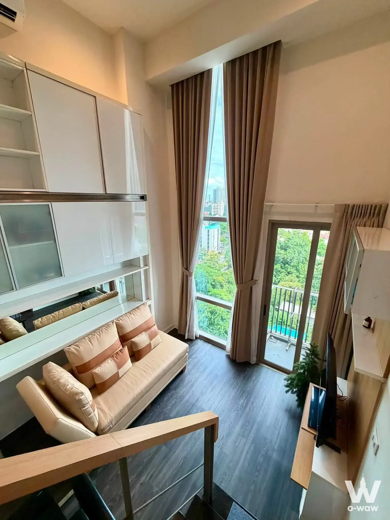 Ideo Morph 38 loft studio with high ceilings, beige sofa, and balcony view of the pool