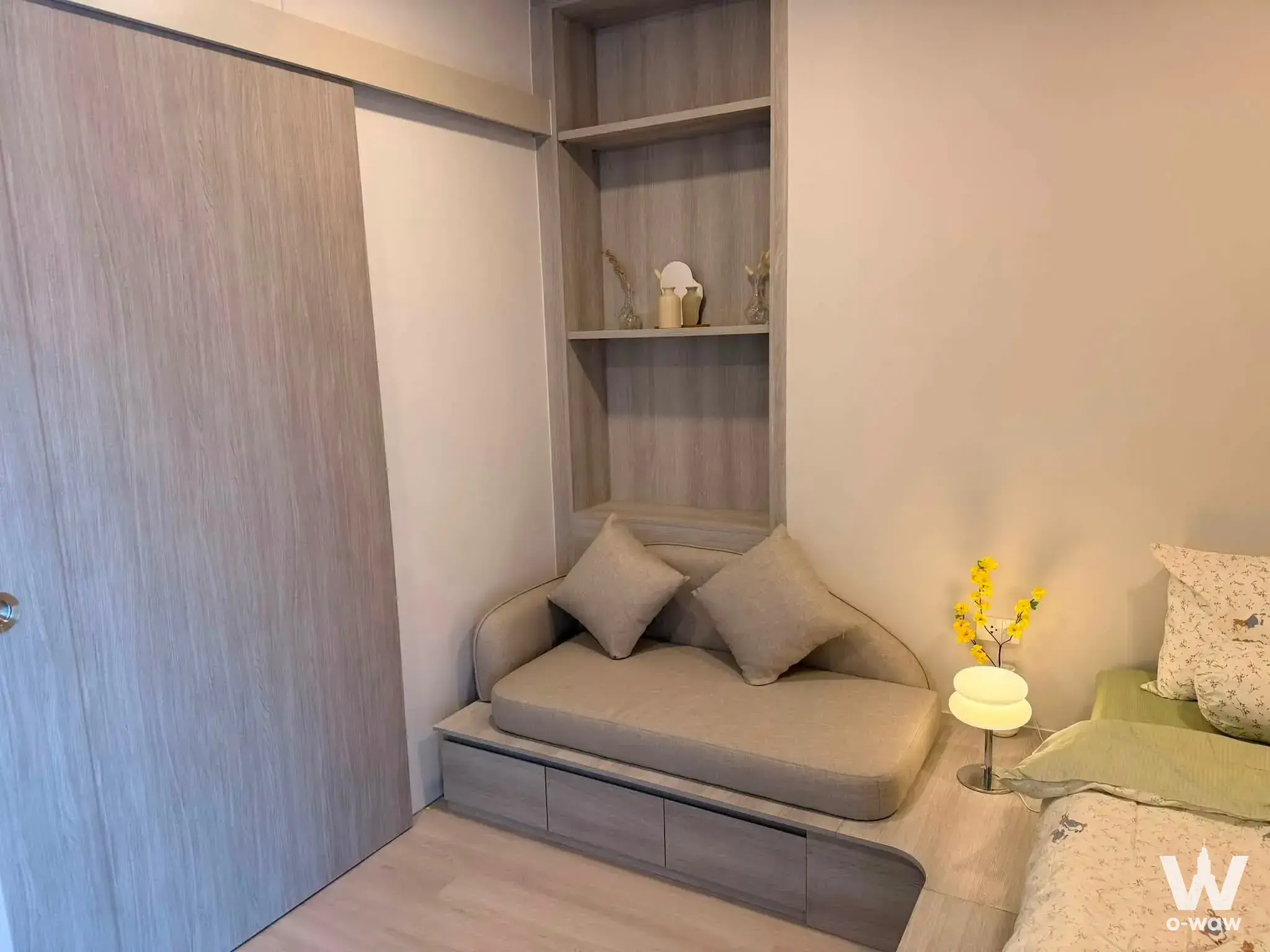 Cozy bedroom in COBE Ratchada-Rama 9 featuring a beige daybed sofa, built-in wood shelving, and warm neutral tones