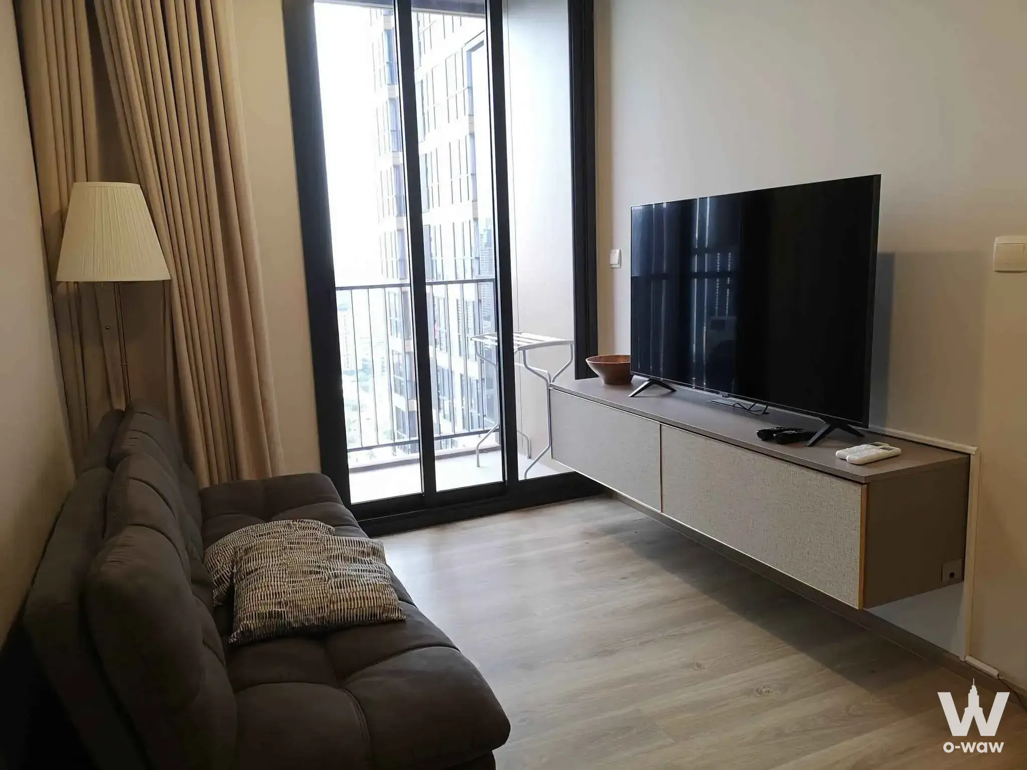 Living room in a 1-bed Oka Haus condo featuring a brown sofa and balcony city views