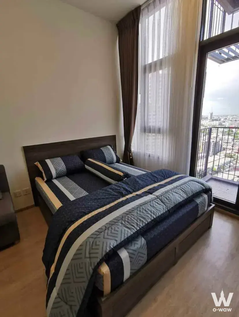1-bed condo for rent in Centric Ratchayothin bedroom with navy duvet, dark wood frame, and city view from balcony