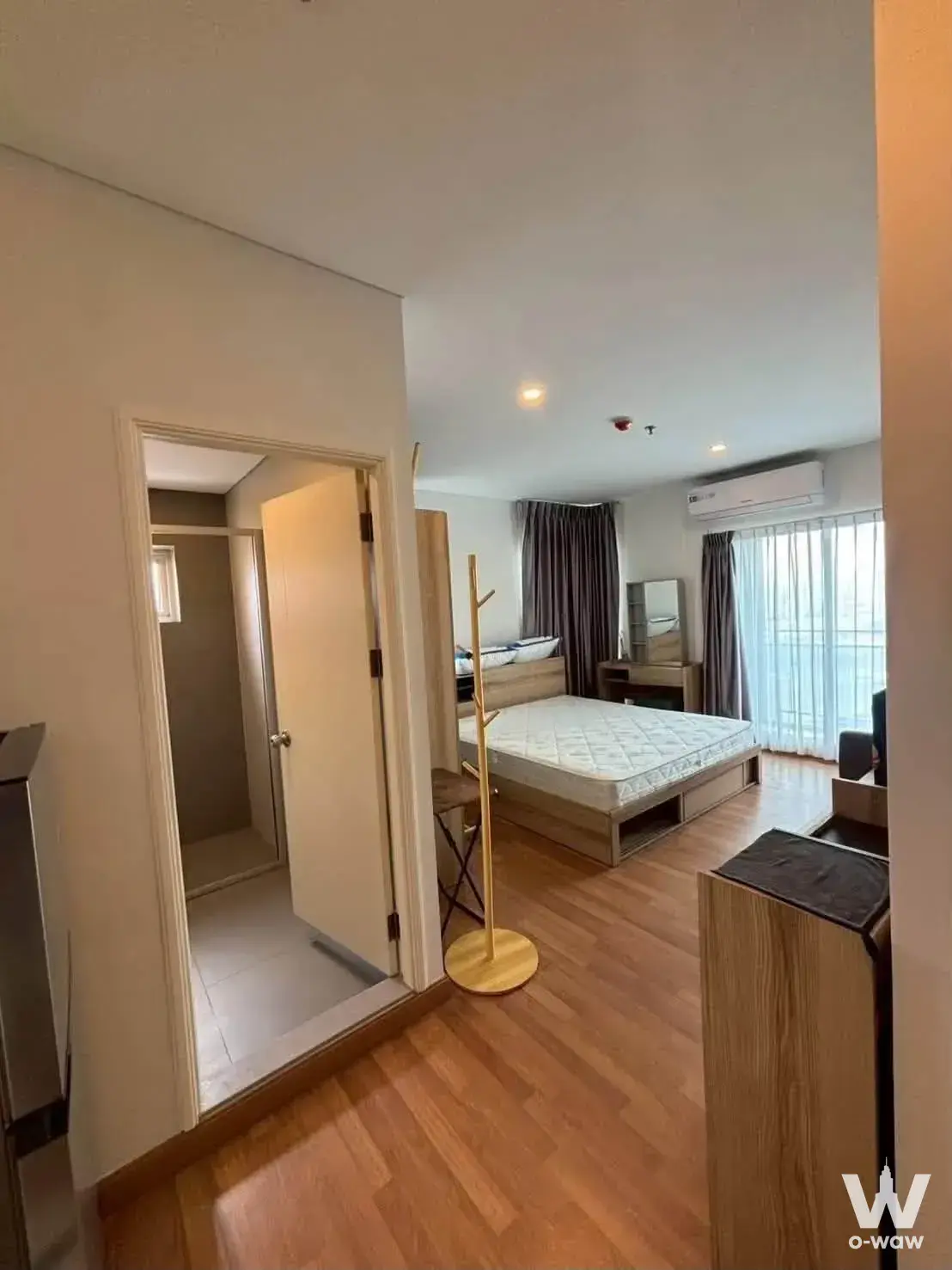 Bright bedroom in Lumpini Place Rama 3 with light wood floors, queen bed, and dark grey curtains